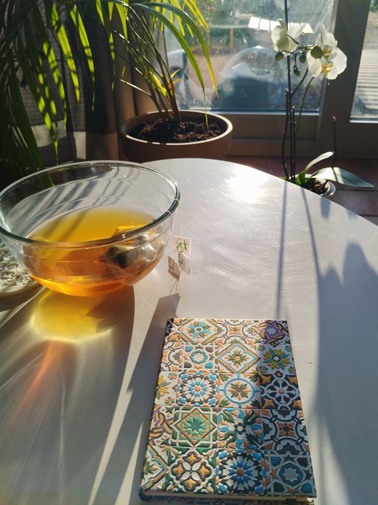 Un bol de thé dans la lumière du matin, à côté d'un carnet coloré